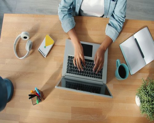 A person working comfortably on a laptop at a bright wooden desk